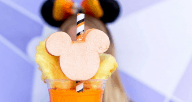 Vibrant orange drink with Mickey-shaped apple slice, pineapple, and striped straw; Mickey ears in the background at Disney World.