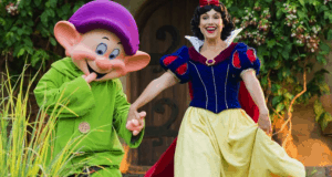 Snow White and Dopey share a joyful moment hand in hand in the lush gardens at Storybook Dining, Disney’s Artist Point.