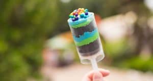 Hand holding a colorful push pop dessert topped with candy, set against lush greenery—just like treats at Disney’s Animal Kingdom.