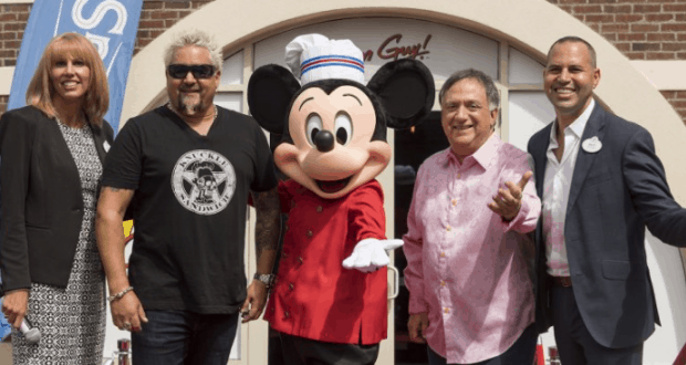 Mickey Mouse in a chef outfit beams with fans outside Chicken Guy at Disney World, capturing a magical moment together.