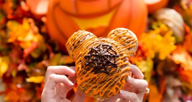 Mickey-shaped pastry with orange icing and chocolate, shown against autumn leaves and a pumpkin at Walt Disney World in fall.