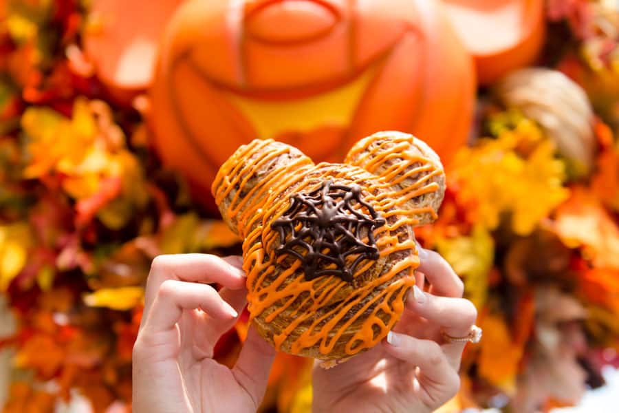 Mickey-shaped pastry with orange icing and chocolate, shown against autumn leaves and a pumpkin at Walt Disney World in fall.