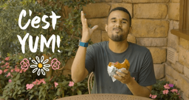 A guest relishing a theme park snack, joyfully gesturing “C’est YUM!” with whimsical flowers—pure foodie fun at Disney World.