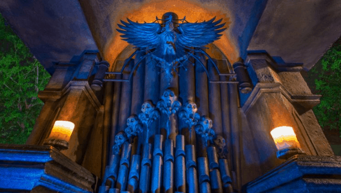 Gothic organ glowing blue, skull pipes and winged statue centerstage, candles flicker—classic Haunted Mansion vibes.