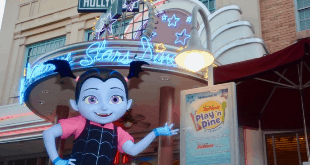 Vampirina greets guests outside the neon Play 'n Dine at Disney’s Hollywood Studios, glowing with playful Disney energy.