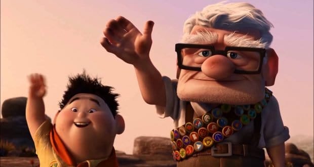 An elderly man and a young Disney fan with pins wave and smile at sunset, radiating that signature Disney park magic.
