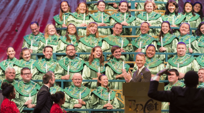 The Epcot Candlelight Processional shines, with a choir in green robes and a guest narrator at the podium leading the tradition.