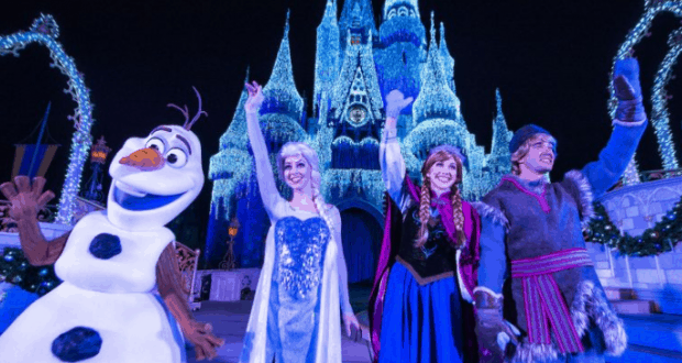 Anna, Elsa, Kristoff, and Olaf wave in front of a sparkling blue Cinderella Castle during Frozen’s magical lighting at Disney World.