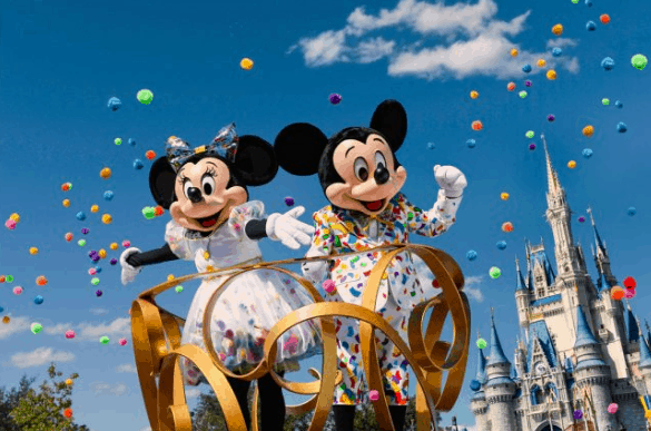 Mickey and Minnie shine in vibrant costumes atop a parade float with confetti, celebrating near Cinderella Castle at Disney World.