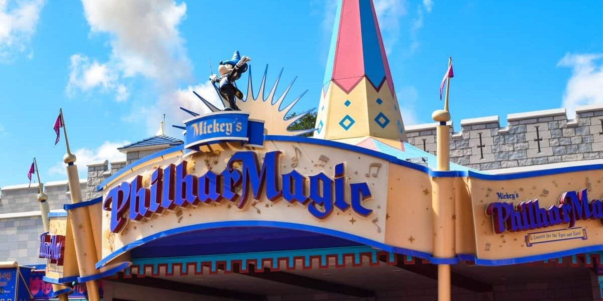 Entrance to Mickey’s PhilharMagic attraction at Disney, featuring a colorful sign with gold and blue lettering and a statue of Mickey Mouse in a sorcerer’s outfit holding a conductor’s baton on top.