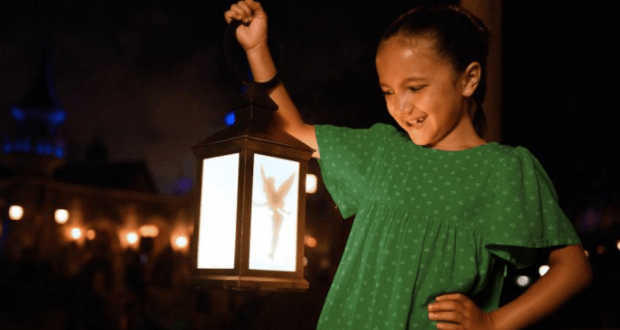 Tinker Bell in her green dress beams, holding a glowing fairy lantern at night—magically captured by PhotoPass at Disney World.