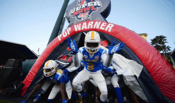 Pop Warner Super Bowl athletes in blue and white rush from an inflatable tunnel onto the field at Walt Disney World.