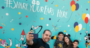 Guests snap a selfie at the vibrant Disney Ear Wall in Walt Disney World, surrounded by colorful balloons and beloved characters.