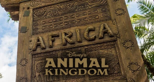 A wooden sign carved with geometric patterns and the word "AFRICA" stands among tropical trees, representing Africa at Animal Kingdom, with the "Disney's Animal Kingdom" logo overlaid at the bottom.