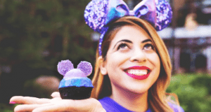 A guest sports purple Mickey ears and shows off a matching cupcake—Disney Parks’ ultimate Purple Treat for foodie fans!.