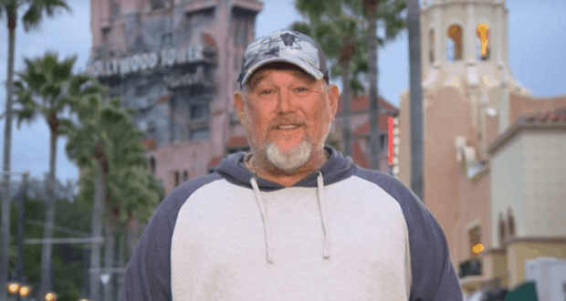 A theme park guest in casual attire grins amid palm trees and city towers, ready for adventure like at Disney or Racing Academy.