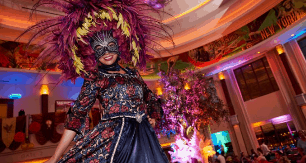 A guest in a dazzling feathered mask and ornate costume celebrates Mardi Gras at Disney Springs’ vibrant indoor festivities.