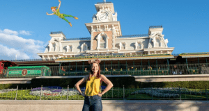 A guest beams at the Magic Kingdom entrance as Peter Pan flies overhead in a whimsical Disney PhotoPass Magic Shot experience.