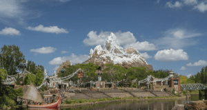 Expedition Everest’s snowy peak rises above the shimmering river, a boat gliding by under vibrant blue skies in Animal Kingdom.