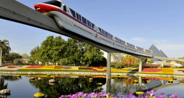 The Disney World monorail soars over vibrant gardens and a sparkling pond, capturing the magic of the park on a sunny day.