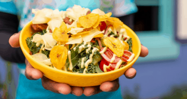 A yellow bowl of fresh salad topped with chips and drizzled with dressing, a must-try treat for Disney Parks food lovers.