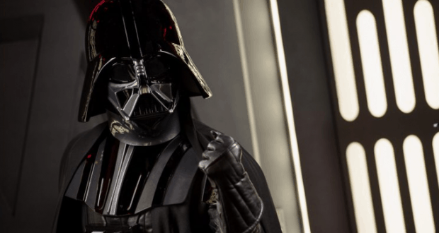 Darth Vader in iconic black armor greets fans inside Epcot at Galactic Gathering, raising a gloved hand for a classic photo op.