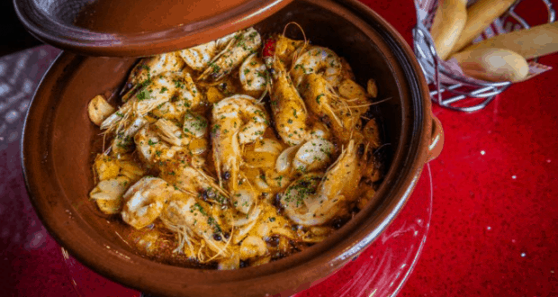 Shrimp and herbs sizzle in a clay pot beside breadsticks on a red table at Jaleo, Disney Springs’ lively dining hotspot.