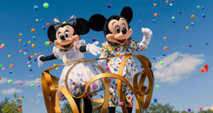 Minnie and Mickey Mouse, dressed in vibrant costumes, wave from a parade float as confetti rains down at Walt Disney World.