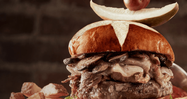 The Edison’s Prime Pretzel Twist Burger of the Month piled high with toppings, fries on the side, ready for your Disney Springs feast.