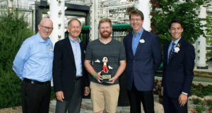 Five friends smile in a Disney World greenhouse, one proudly holding a Mickey Mouse trophy after the Behind the Seeds Tour.