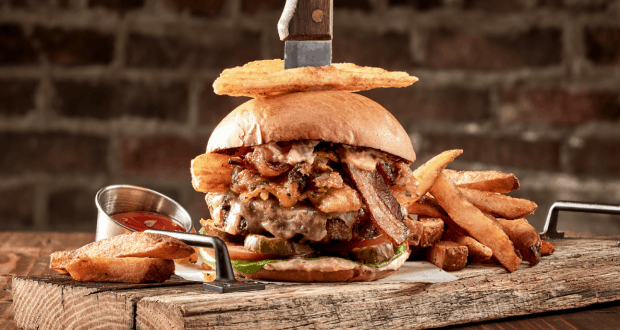 The Edison’s BBQ Tavern Burger at Disney World boasts bacon, onion rings, fries, and a knife in the bun on a wooden board.