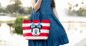 Stylish guest in a denim dress shows off her Minnie Mouse tote by the lake, ready for festive shopping at Disney Springs, Disney World.