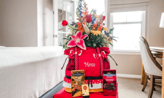 A Disney Floral & Gifts red "Mom" bag with flowers and chocolates sits in a sunlit resort room, perfect for Mother's Day magic.