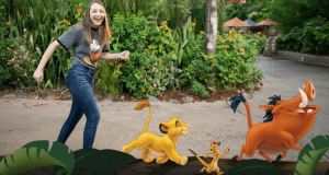 Guest shares a joyful PhotoPass moment with Simba, Timon, and Pumbaa from The Lion King in a vibrant Disney park setting.