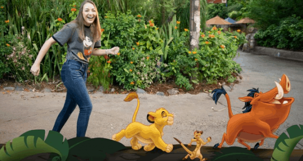 Guest shares a joyful PhotoPass moment with Simba, Timon, and Pumbaa from The Lion King in a vibrant Disney park setting.