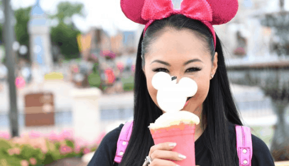 A Disney fan in pink Minnie ears enjoys an Imagination Pink drink with Mickey Mouse topper, beaming at Walt Disney World.