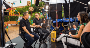 Three movie creators chat and share photos behind the scenes at Universal Studios, enjoying a lively break from filming outdoors.
