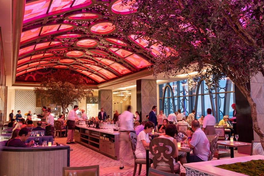 Chic dining spot with a glowing pink glass ceiling, bustling guests, and indoor trees—ideal for magical New Year’s Eve near Disney World.