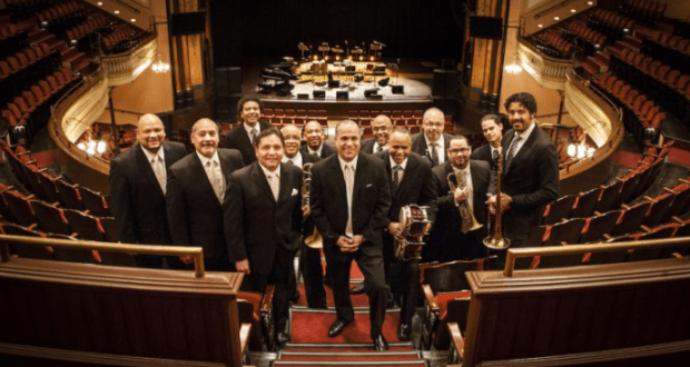A jazz band in sharp suits lines theater stairs, ready to entertain like the Spanish Harlem Orchestra at a theme park show.