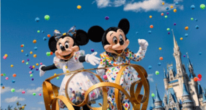 Mickey and Minnie Mouse in vibrant costumes wave on a confetti-filled parade float by Cinderella Castle at Walt Disney World.
