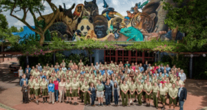 Zoo staff and animal care experts pose by a colorful animal mural at the park for Zoo Keeper Week, honoring their vital role.