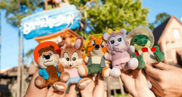 Fans showing off Splash Mountain Wishables plush toys in front of the vibrant Walt Disney World entrance sign.