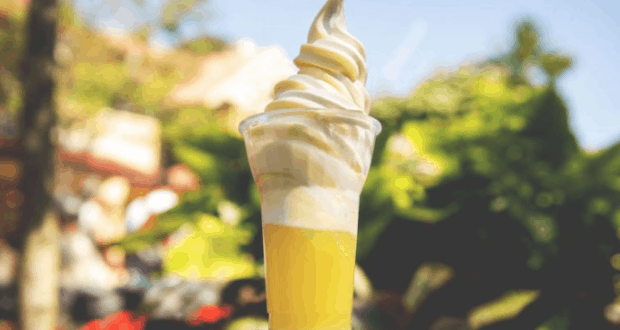 Pineapple Dole Whip in a cup, perfectly swirled and ready to enjoy, served with lush Disneyland scenery in the background.
