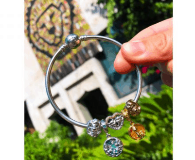 Pandora charm bracelet sparkling in front of Disney mosaic architecture, surrounded by lush greenery and park enchantment.