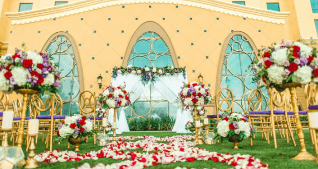 Magical outdoor wedding at Disney’s Coronado Springs, with vibrant florals, rose petals, and a festive arch by the yellow resort building.