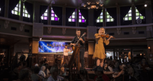 Live Irish music on stage inside Raglan Road Pub, with stained glass windows and festive crowds celebrating the Great Irish Hooley.