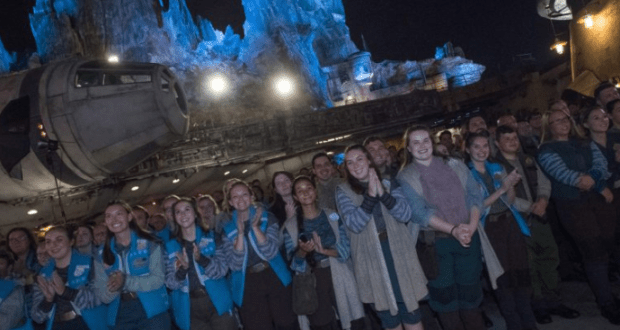 Cast Members in Star Wars costumes cheer and celebrate at night in front of the Millennium Falcon at Galaxy's Edge, Disney World.