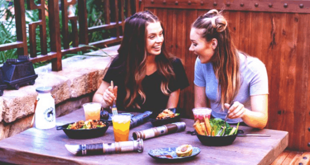 Guests savoring Star Wars-inspired cuisine and drinks at an outdoor table in Galaxy’s Edge, smiles reflecting Disney magic.