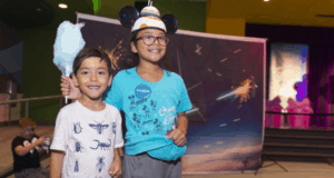 Two kids beam at Disney World; one enjoys blue cotton candy, the other sports Mickey ears and a Galaxy’s Edge hat—pure magic!.
