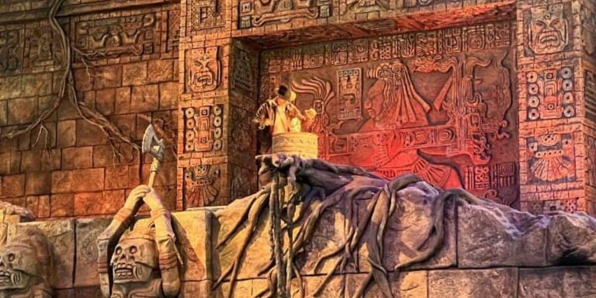 A detailed ancient temple wall with intricate carvings and symbols. A sculpture of a figure holding a staff stands atop a rock formation. The scene is lit with warm, dramatic lighting, highlighting the carvings and textures.